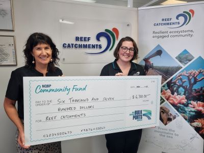 Two women holding a check for $6700. There are Reef Catchments signs in the background.
