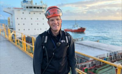 Man standing on a ship with a tug in the background.